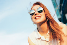 Positive Beautiful Happy Red Haired Girl In The Mirror Sunglasses On Blue Sky Background, Summer Sunset Time