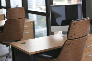 Wall Mural - selective focus at wooden table desk in office business room with big computer monitor and windows background