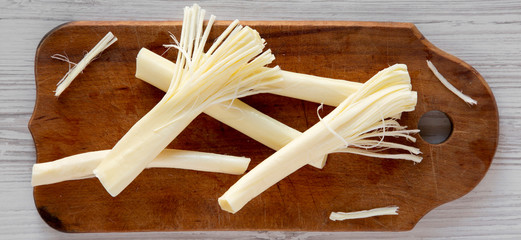 String cheese on rustic wooden board over white wooden surface, top view. Healthy snack. Flat lay, overhead, from above.