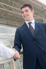 Wall Mural - Happy successful professional meeting colleague in office corridor. Young man in formal jacket and tie shaking hands with coworker. Handshake concept