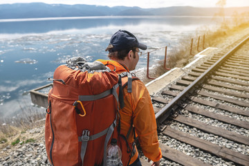 Tourist Hiking with an orange backpack is on the old railway at the foot of the mountain. Travel to lake Baikal