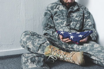 Wall Mural - Partial view of depressed man in military uniform sitting on grey floor in corner and holding USA national flag