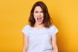 © sementsova321 - Screaming emotional angry woman isolated over yellow studio background. Half length portrait of young brunette female wearing white casual t shirt. Human emotions and facial expression concept.