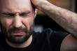 depressed bearded man crying with closed eyes and holding hand on head