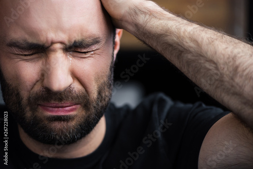 Fotomural depressed bearded man crying with closed eyes and holding hand on head
