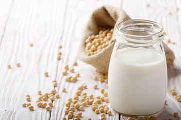 Poster - Non-dairy alternative Soy milk or yogurt in mason jar on white wooden table with soybeans in hemp sack