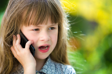 Cute child young girl talking on cellphone outdoors. Children and modern technology, communication concept.