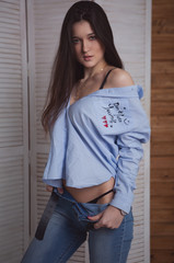 very sexy brunette in a sexy pose with unbuttoned shirt and jeans, she looks at the camera with a charming expression on her face