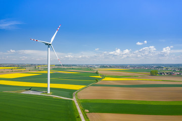 Aerial view of wind turbine. Rapeseed blooming. Windmills and yellow fields from above. Agricultural fields on a summer day. Renewable Energy.