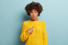 Image Of Amazed Indignant Surprised Young Lady Has Curly Afro Hairstyle, Being Speechless, Points At Herself, Wears Yellow Sweater, Asks Why Me, Isolated Over Blue Background, Stares Concerned.