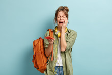 Depressed Dejected Female Cries Holds Mobile Phone, Has Problem With Internet Connection, Checks Email, Has Bag On Shoulder, Dressed Casually, Isolated Over Blue Background. Negative Emotions