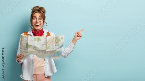Fotomural Smiling optimistic young European female guide holds map, shows direction to tou
