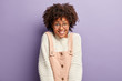 © wayhome.studio - Portrait of charming girl with Afro hair, pleased facial expression, smiles broadly, shows white teeth, has pleasant appearance, dressed in loose sweater and pink overalls, enjoys relaxing day