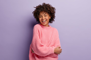 Poster - Sincere gentle feminine model expresses positive emotions and feelings, being glad to pose on camera for making photo, dressed in oversized pink sweater, shows white teeth, has healthy skin.