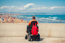 Lonely Man On Electric Wheelchair Looking  At The Beach. Disabled Person At The Beach.