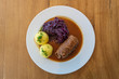 Rinderroulade, Beef roll or roulades, traditional german meal, thin meat wrap bacon, onion and pickle, serve with pickled red cabbage, dumplings potatoes and sauce on white plate and wooden table.