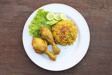 Wall Mural - Muslim yellow rice with chicken in a white plate on a wooden floor