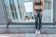 © byswat - Girl stands glass case, summer city woman fitness sport, active lifestyle youth. Motivation power, achievement, success. Free space. Phone tattoos fitness bracelet sportswear, leggings, top sneakers.