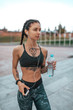 © byswat - Woman athlete girl hand water bottle fitness workout, city, motivation power tattoo. Active lifestyle, mobile phone, headphones, online Internet listening music. Sportswear top. Rest after exercise.