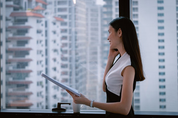 Business Woman talking with mobile phone  in Modern office building and looking documents in another hand with city in background