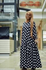 Wall Mural - Smiling young islamic African woman wearing fashionable headscarf and dress standing on a metro train station with a bag in her hand