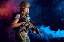 Female Storm Trooper In Military Camouflage Uniform Protected With Helmet, Body Armour With Submachine Gun Seeking Aims In The Smoky Darkness