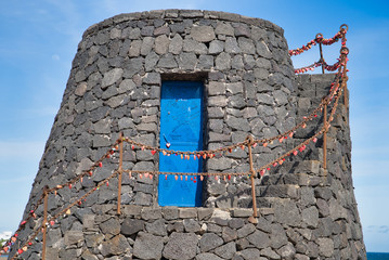 Wall Mural - Tower of black lava stones, blue door and love locks on Promenade of Playa grande in Puerto del Carmen, Lanztarote, Spain