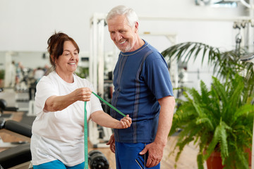 Wall Mural - Beautiful elderly couple at sport club. Happy senior lady with measuring tape showing her fitness results at fitness club. People, sport, diet and weight loss concept.