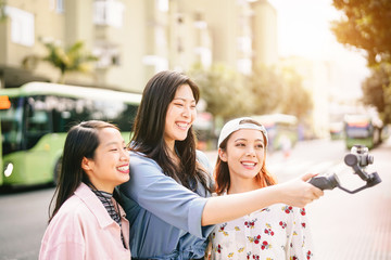 Wall Mural - Happy Asian girls making video stories in the city center - Trendy young friends filming with gimbal smartphone  outdoor - Friendship, technology, youth people lifestyle and social media concept
