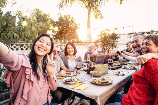 Happy family cheering and toasting with red wine glasses at dinner outdoor - People with different ages and ethnicity  having fun at bbq party - food and drink, retired and young people concept
