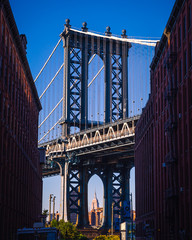 Manhattan bridge seen from a narrow alley enclosed by two brick buildings on a sunny day in summer