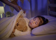 © DN6 - Mother putting blanket on and stroking head for her little girl daughter on bed in a dark bedroom at night, Child asian girl hug teddy bear, Comfortable children at home concept