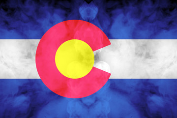 The national flag of the US state Colorado in against a gray smoke on the day of independence in different colors of blue red and yellow. Political and religious disputes, customs and delivery.