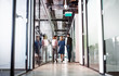 © Halfpoint - Rear view of group of business people walking in an office building, talking.