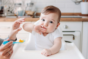 Wall Mural - Charming little baby boy 6-8 months eating first food pumpkin from spoon at home