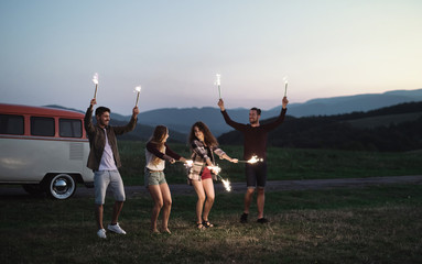 Wall Mural - A group of friends with sparklers standing outdoors at dusk.