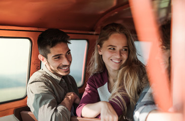 Wall Mural - A group of young friends on a roadtrip through countryside, sitting in a minivan.