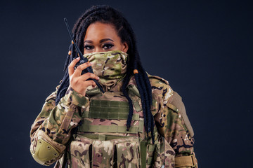 Woman in a military camouflage with a radio afro american army latin soldier in camouflage clothes hair dreadlocks evening makeup on a black background in the studio.