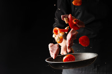 chef prepares meat with vegetables, on a black background, roasting, tasty food, recipe book, menu, restaurant business