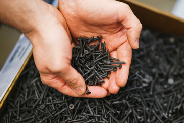 Man holds in his hands many black small screws for repair and fasteners in a box close-up.