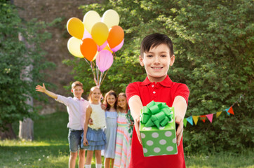 Wall Mural - childhood and people concept - smiling little boy in red polo t-shirt with gift box at birthday party over friends in summer park background