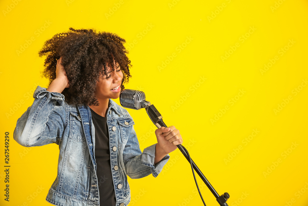 African-American girl with microphone singing against color background