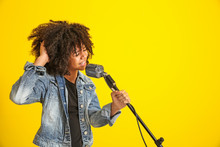 African-American Girl With Microphone Singing Against Color Background