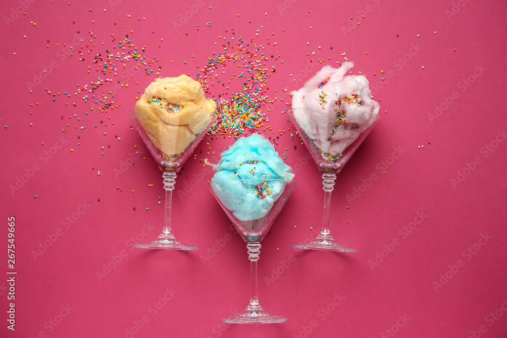 Glasses with tasty cotton candy and sprinkles on color background