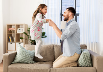 Poster - family, childhood and fatherhood concept - happy father and little daughter jumping on sofa and having fun at home