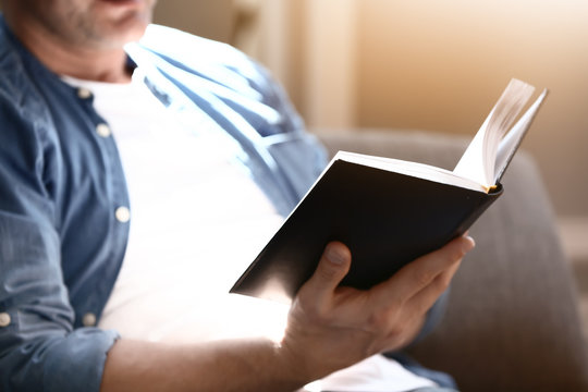 Handsome mature man reading book at home, closeup