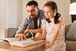 © Syda Productions - education, family and homework concept - happy father and daughter with book writing to notebook at home