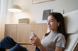 © D'Action Images - Cute teenage girl sitting on armchair at home and using mobile phone with headphones