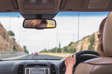 The girl is driving on the highway in Australia. View from the back seat of the car on the windshield, road and the driver