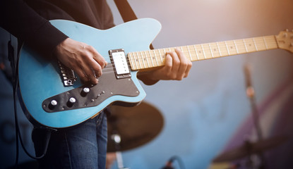 The guitarist performs a melody on a blue electric guitar, which is connected by a wire to the equipment, on a blue background.